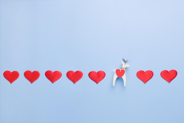 Una fila de corazones sobre un fondo azul con una pequeña figura de un ciervo blanco Espacio de copia