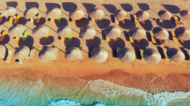 Fila de guarda-sóis de palha na praia de areia Cenário de praia tropical com guarda-sóis Vista de cima da paisagem marítima