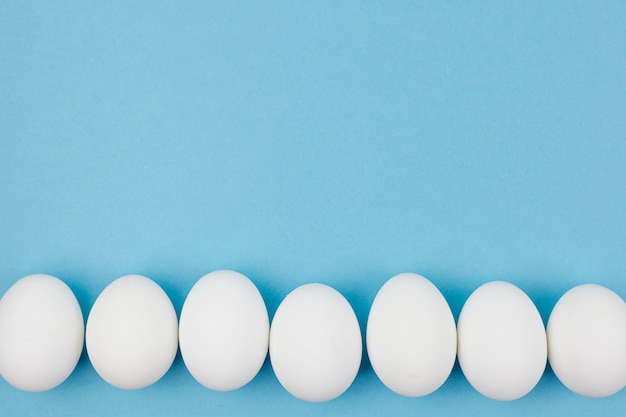 Foto fila de ovos de galinha branca na mesa azul