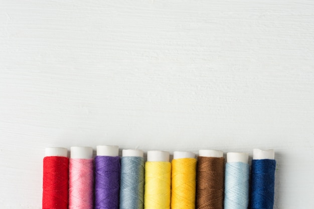 Fila de hilos de coser multicolores en carretes de cartón. Fondo de madera blanca