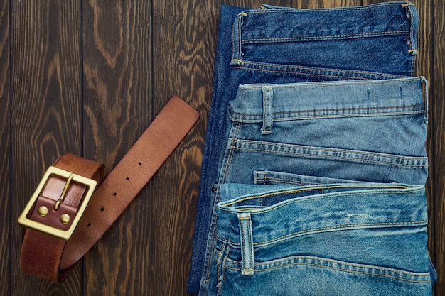 Fila de jeans para hombre y cinturón de cuero sobre fondo de madera, vista superior