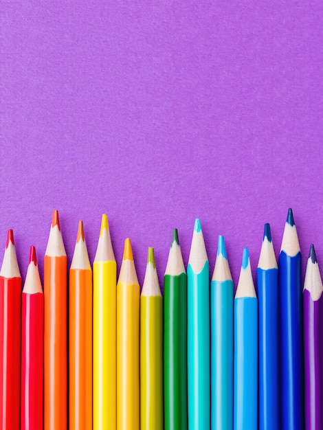 Fila de lápices de colores acuarela sobre fondo lila. Suministros escolares