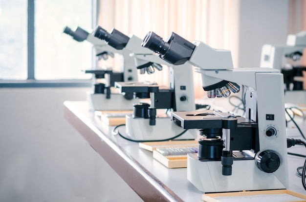 Fila del microscopio con placa micro en la mesa blanca en entorno de laboratorio para la investigación y el aprendizaje