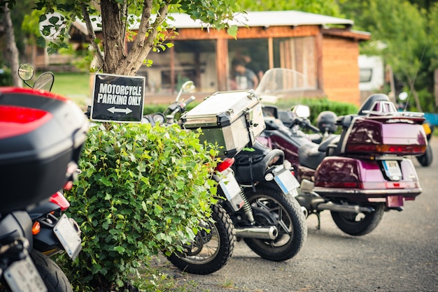 Una fila con motocicletas estacionadas en un área de campamento con un letrero de "Solo estacionamiento de motocicletas".