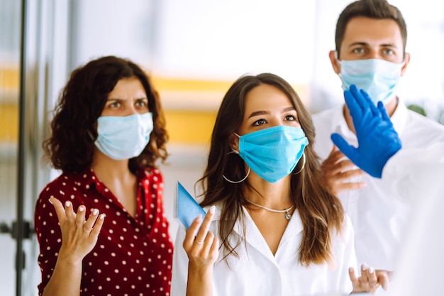 ? Fila de personas con máscaras médicas en la entrada de la oficina. COVID-19.