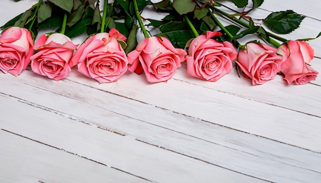 Una fila de rosas rosadas en una mesa de madera blanca