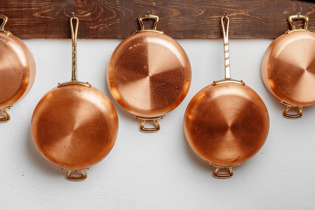 Fila de sartenes de cobre limpias y brillantes de diferentes tamaños colgadas sobre una plancha de madera