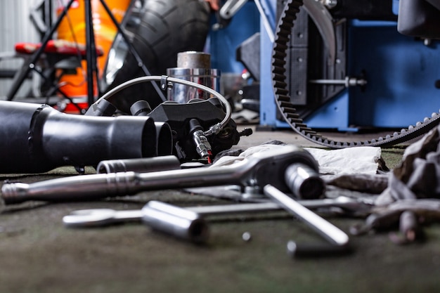 Fila de tornillos y herramientas de llave inglesa en un piso en el taller cerca de la bicicleta vieja reparada o motor de motocicleta. Escena industrial con equipamiento