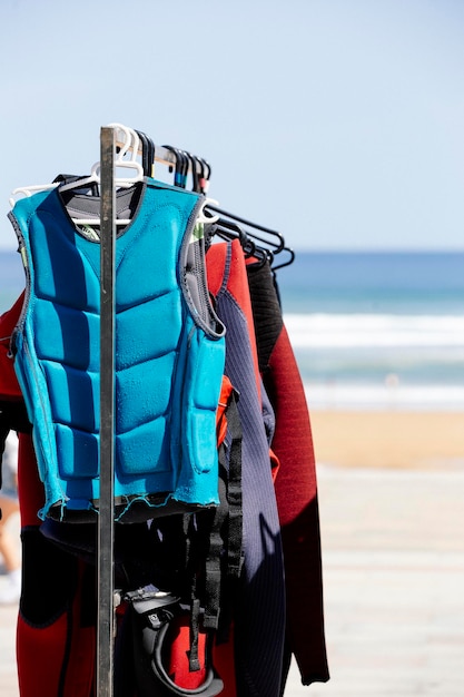 Una fila de trajes de neopreno colgando de un estante en una imagen de retrato de la escuela de surf