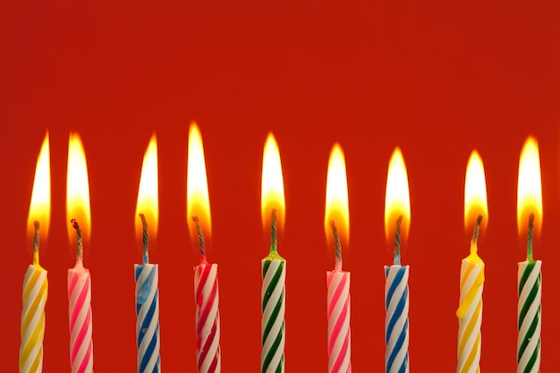 Una fila de velas de cumpleaños coloridas encendidas sobre un fondo rojo