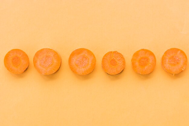 Fila de zanahorias frescas en rodajas sobre fondo naranja