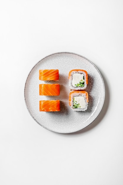 Filadelfia rollos con salmón, pepino y queso en un plato sobre fondo blanco.