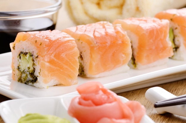 Filadélfia rolo sushi em um prato branco com molho de soja wasabi e gengibre