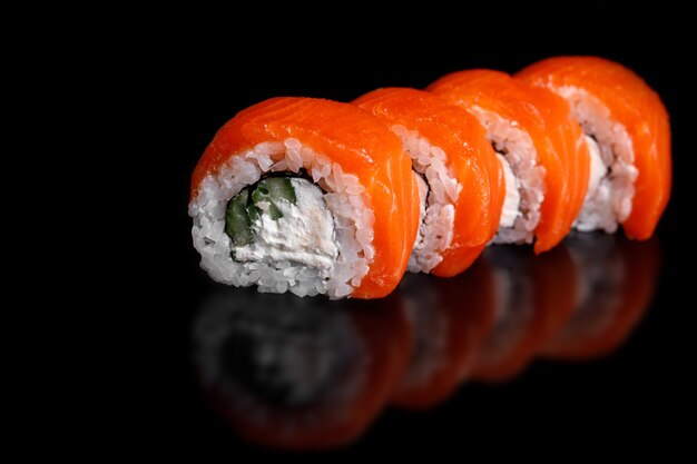 Filadélfia Sushi Roll em uma superfície preta com reflexão.