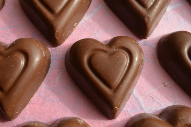 Foto filas de doces de coração de chocolate em papel rosa