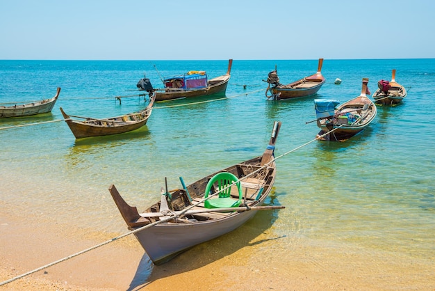 Filas de muchos barcos tradicionales de pesca de madera de cola larga amarrados en la playa de arena tropical con rocas