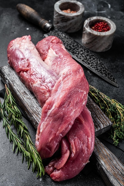 Filé cru de carne de porco de lombo cru em tábua de madeira com ervas fundo preto vista superior