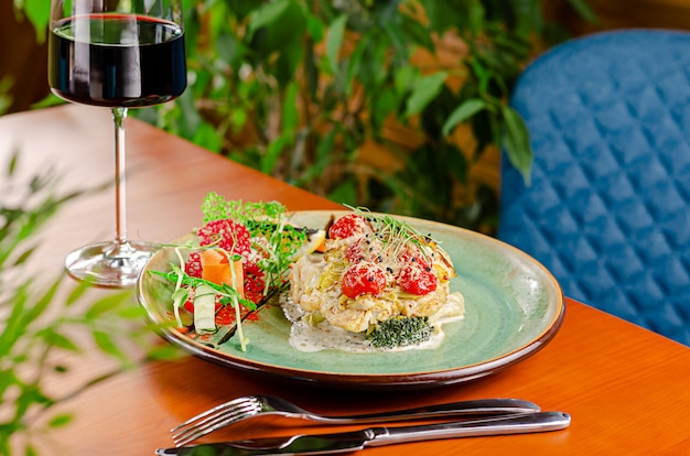 Filé de bacalhau com tomate cereja e queijo, servido com legumes e vinho tinto. Conceito de comida mediterrânea