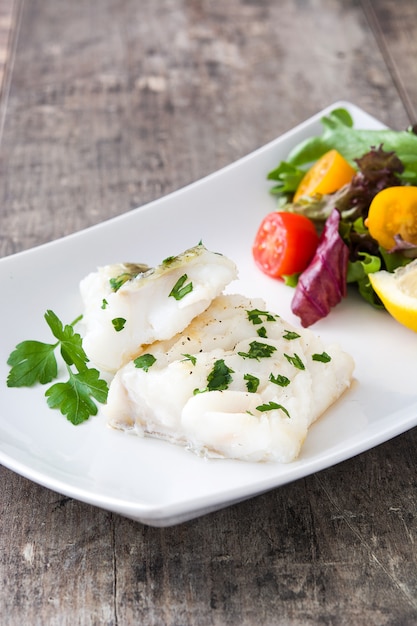 Filé de bacalhau frito e salada na mesa de madeira