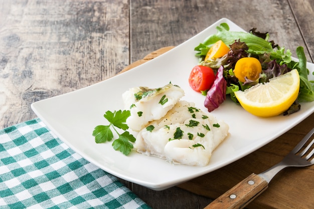 Filé de bacalhau frito e salada na mesa de madeira