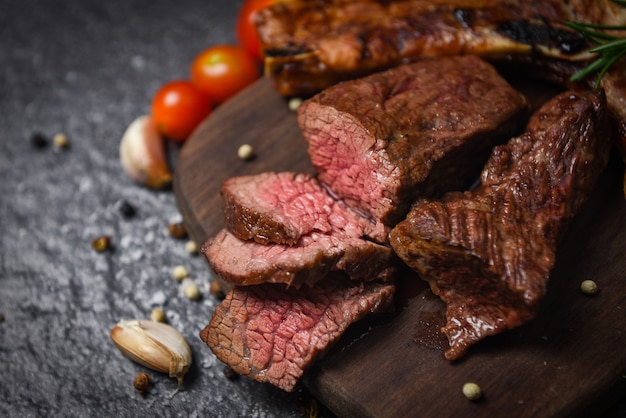 Filé de bife assado com ervas e especiarias, servido com vegetais na placa de madeira - fatia de carne grelhada na superfície preta