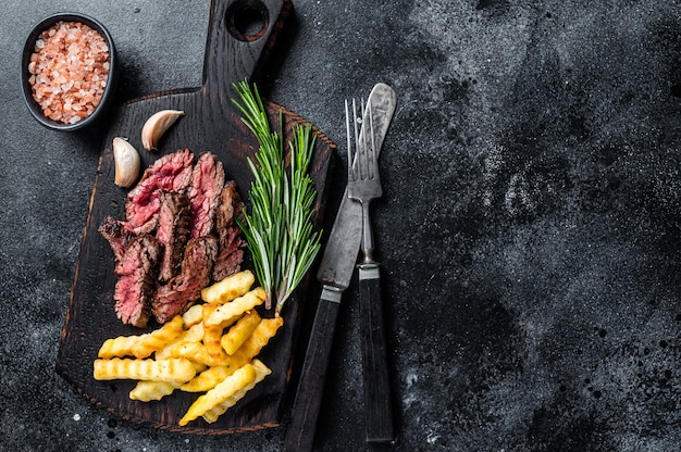 Filé de carne bovina com saia de facão fatiado assado na tábua de madeira com batatas fritas