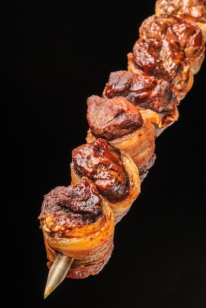 Foto filé de churrasco com bacon no espeto sobre fundo preto gastronomia brasileira