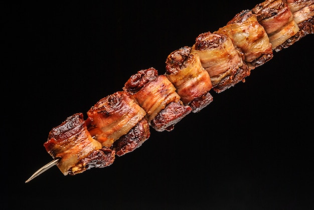 Filé de churrasco com bacon no espeto sobre fundo preto gastronomia brasileira