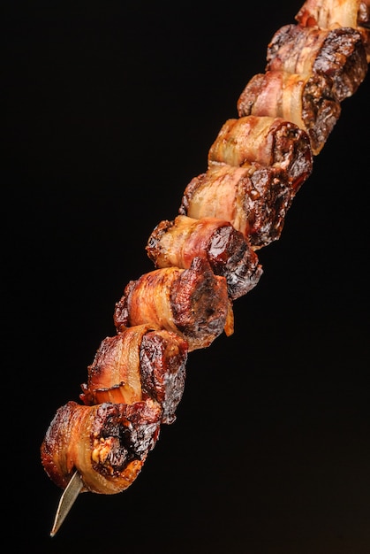 Foto filé de churrasco com bacon no espeto sobre fundo preto gastronomia brasileira