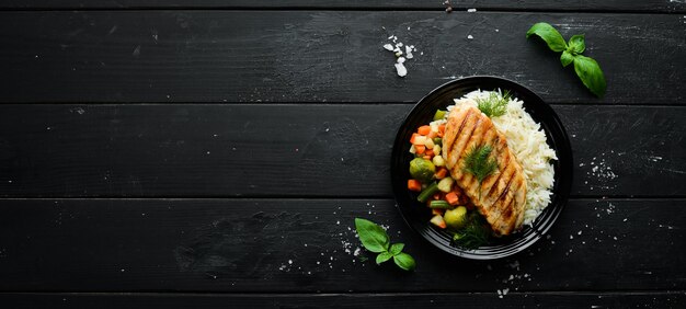 Filé de frango assado com arroz e legumes em um prato preto Vista superior Espaço para cópia grátis