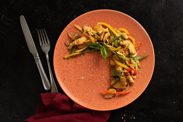 Filé de frango com legumes, pimenta e cebola. Prato com frango em uma mesa preta. Vista do topo.