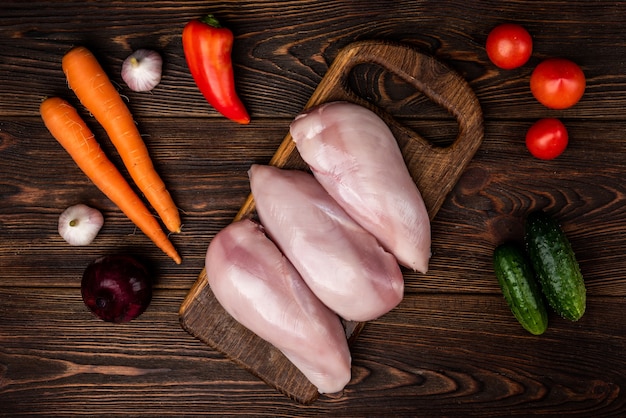 Filé de frango cru na madeira escura com legumes.