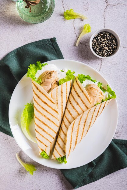 Foto filé de frango grelhado embrulhado em tortilha com alface e molho em um prato e vista vertical