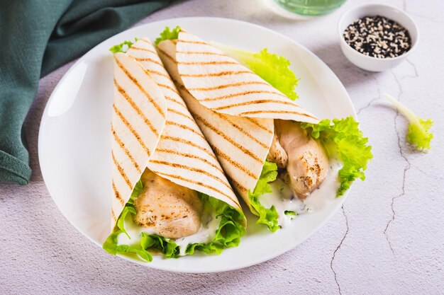 Foto filé de frango grelhado embrulhado em tortilha com alface e molho em um prato na mesa