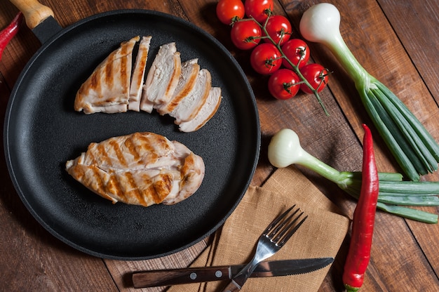 Filé de frango grelhado na frigideira. legumes crus em uma tigela, mesa de madeira