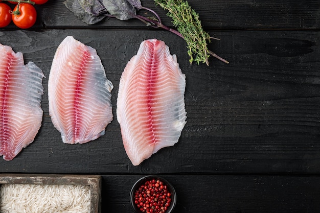 Filé de peixe branco, com ingredientes de arroz basmati e tomate cereja, em mesa de madeira preta, vista superior