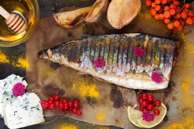 Filé de peixe com mel de legumes e queijo azul em um fundo escuro Cavala grelhada com frutas de limão e flores cor de rosa em papel manteiga Closeup