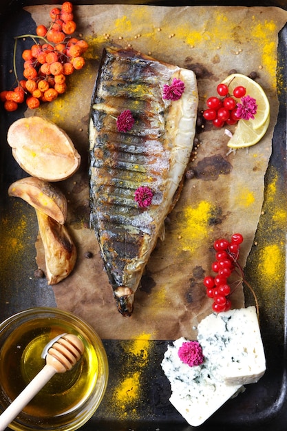 Filé de peixe com mel de legumes e queijo azul em um fundo escuro Cavala grelhada com frutas de limão e flores cor de rosa em papel manteiga Closeup