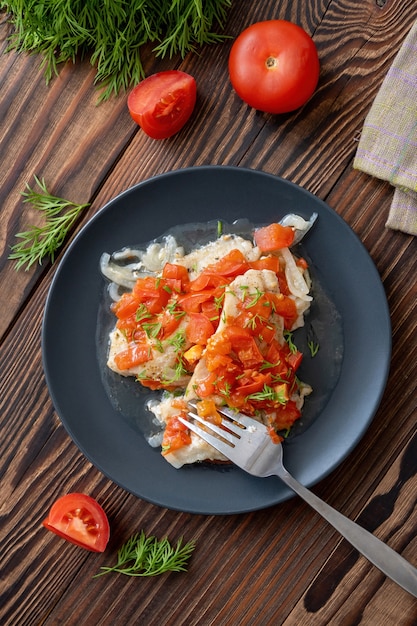 filé de peixe com tomate e endro picado na placa preta na vista de cima da mesa de madeira