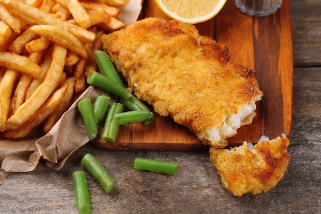 Filé de peixe frito à milanesa e batatas com aspargos e limão na tábua e fundo de madeira rústica