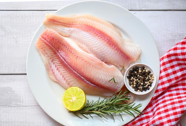 Filé de peixe pangasius cru fresco com ervas e especiarias limão limão e alecrim carne zorra peixe tilápia listrado peixe-gato filé de peixe na chapa branca com ingredientes para cozinhar vista superior