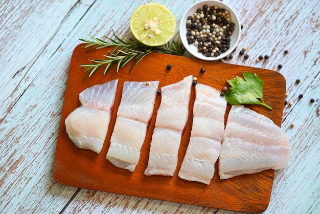 filé de peixe pangasius cru fresco com ervas e especiarias pimenta preta limão limão e alecrim, filé de peixe na placa de madeira com ingredientes para cozinhar, carne dolly peixe tilápia listrado bagre - vista superior