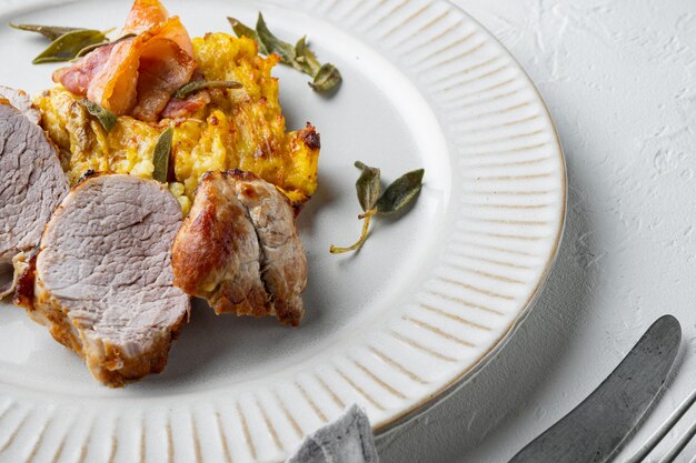 Filé de porco grelhado e purê de batata gratinado com conjunto de sálvia e presunto, no prato, na pedra branca