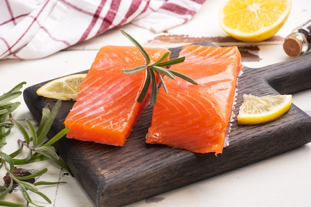 Filé de salmão, peixe salgado vermelho em uma tábua de madeira. Limão, especiarias com alecrim.