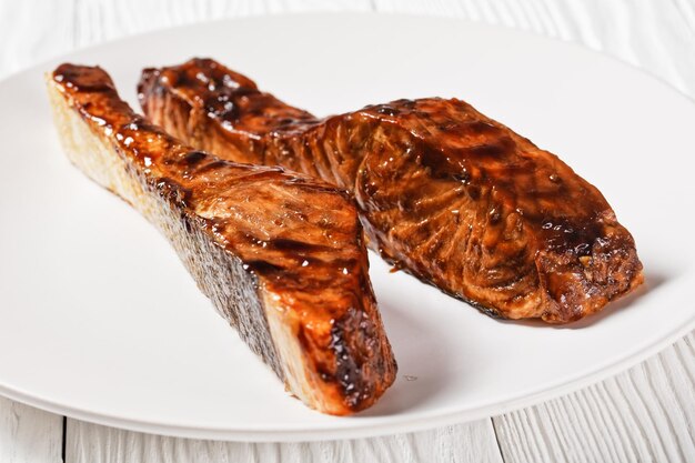 Filé de salmão teriyaki em um prato branco em uma mesa de madeira texturizada closeup