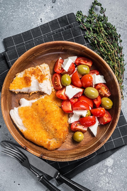 Filé de tilápia frito em um prato com salada Fundo cinza Vista superior