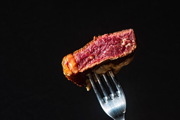Filé mignon espetado no garfo, mostrando a ponta da carne de churrasco no fundo preto. carne mal passada.