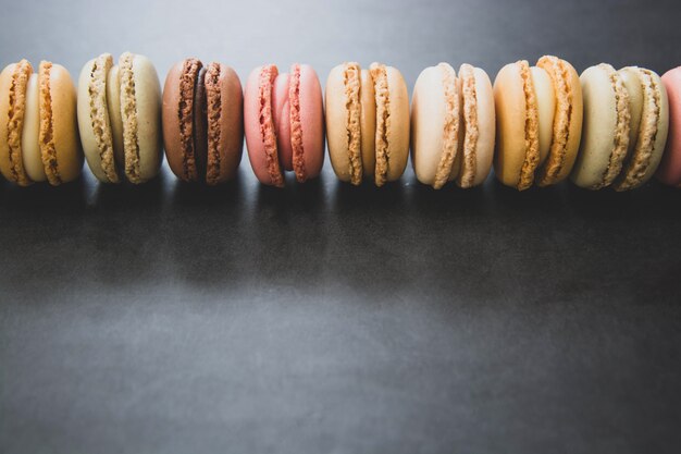 Fileira de bolinhos de amêndoa coloridos franceses sobre a tabela escura, preta com espaço da cópia.