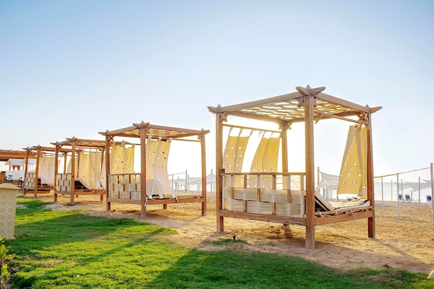 Fileira de móveis de madeira para descanso com cortinas espreguiçadeira cama gazebo na praia de areia com gramado mar tropical resort de luxoFérias de verão no EgitoÁfrica em dia ensolarado quente ao ar livre no sol