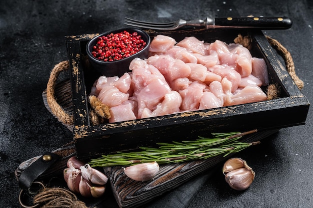 Filés de peito de frango em cubos crus fatiados de carne de aves em bandeja de madeira Fundo preto Vista superior